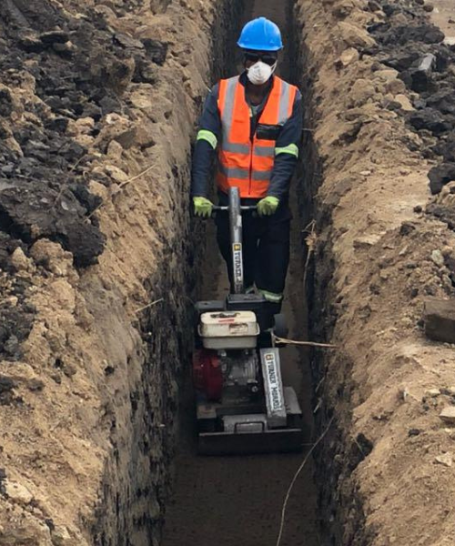 A man in an orange vest and blue helmet working in a trench